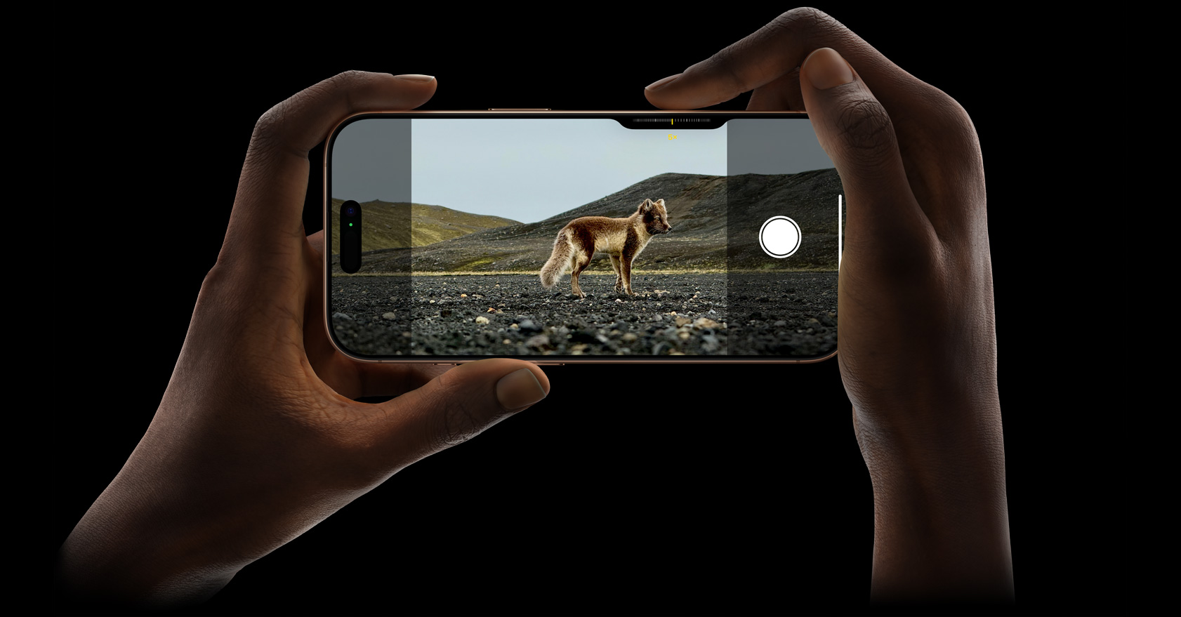 Doua maini tin un iPhone 16 Pro facand o poza intr-un decor salbatic, cu camera cu teleobiectiv 5x